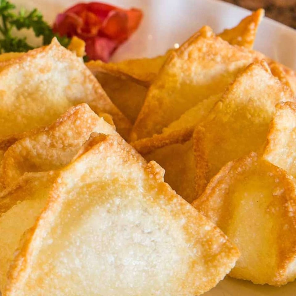 Crispy golden-brown fried wontons, garnished with parsley and a red flower, on a white plate.