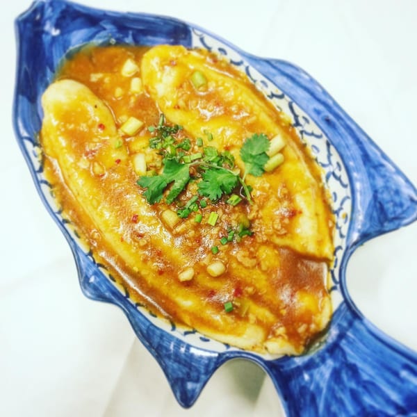 Monark Asian Bistro's steamed fish in a savory sauce, garnished with cilantro and green onions, served in a blue fish-shaped dish.