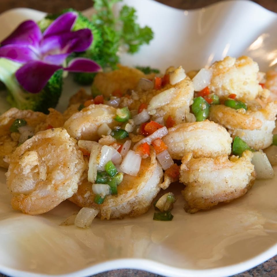 Crispy fried shrimp with diced peppers and onions, garnished with broccoli and a purple orchid.