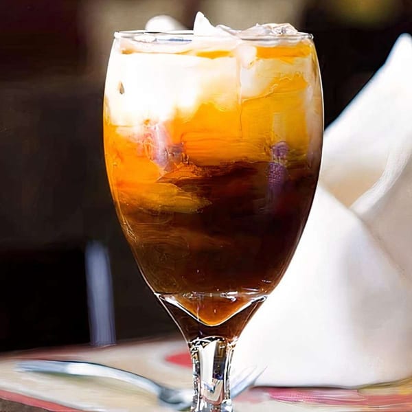 A tall glass of iced Thai tea with distinct layers of dark tea, orange, and white cream.