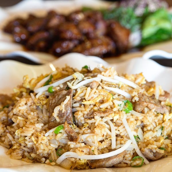 Close-up of beef fried rice with bean sprouts and green onions, with another dish blurred in the background.