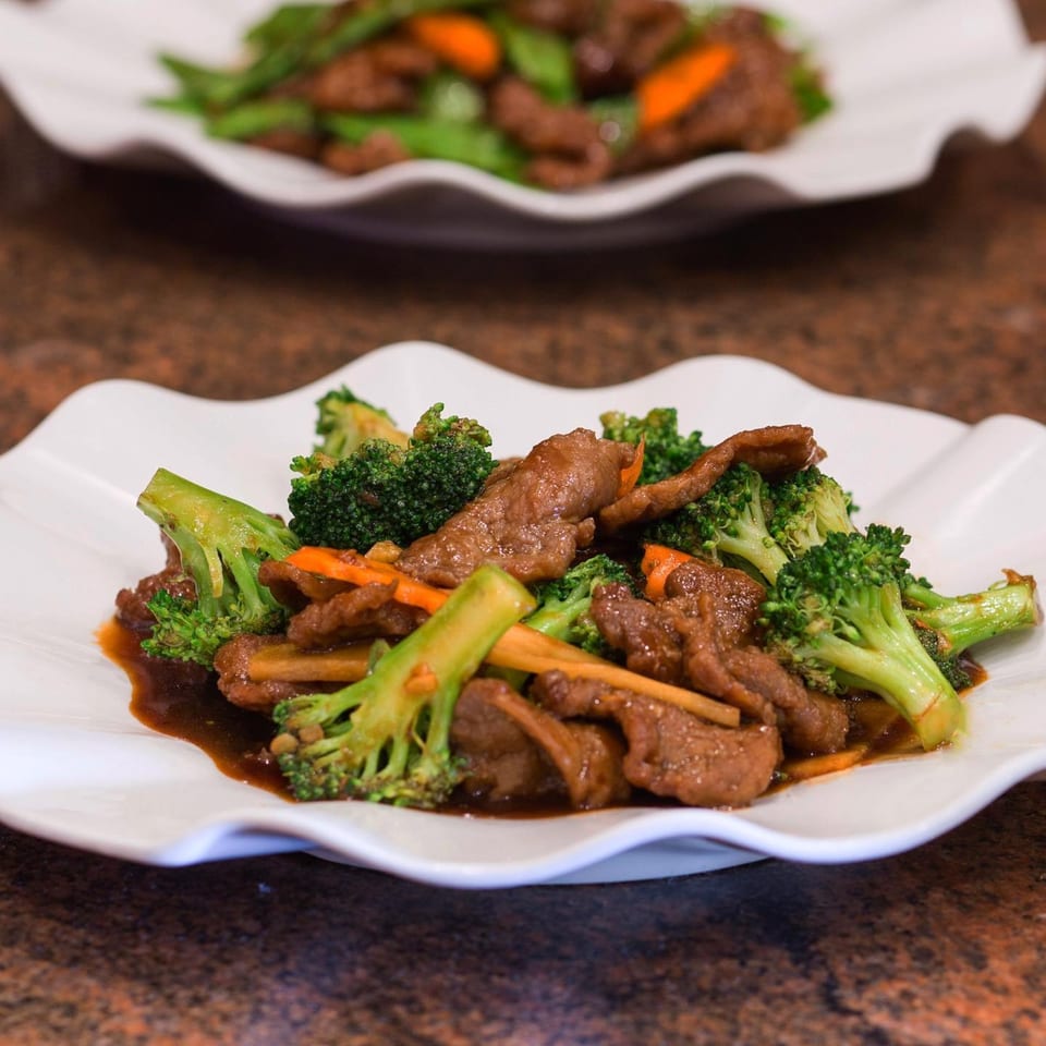 Two plates of Monark Asian Bistro's beef and broccoli stir-fry with carrots in a savory sauce.
