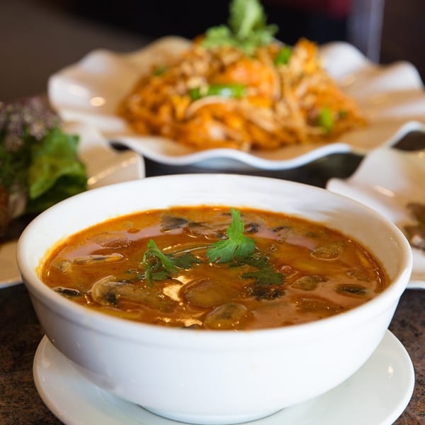 A bowl of Monark Asian Bistro's Chinese soup with mushrooms and cilantro, with noodles in the background.