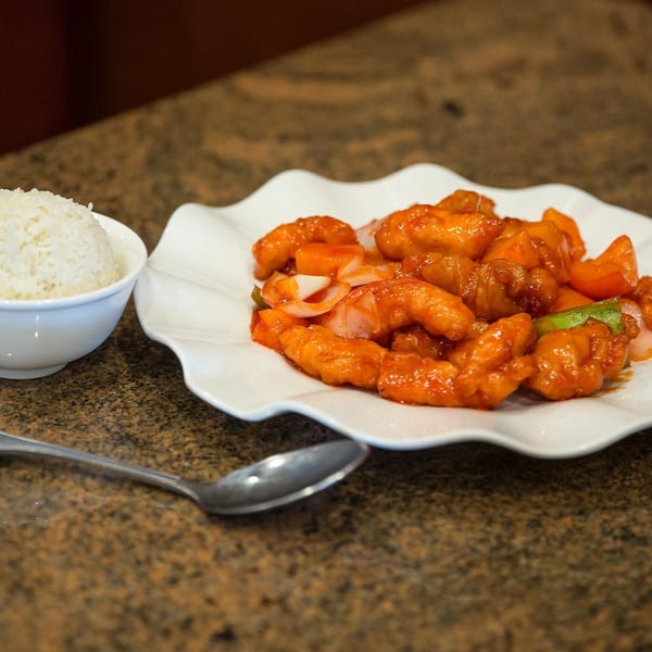 Sweet and sour chicken with bell peppers and onions, served with a side of white rice.