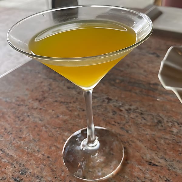 A martini glass filled with a vibrant yellow drink sits on a speckled brown table at Monark Asian Bistro.